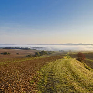 Countryside with pathway and morning mist over the fields at sunrise in the community of Grossheubach in Bavaria, Germany