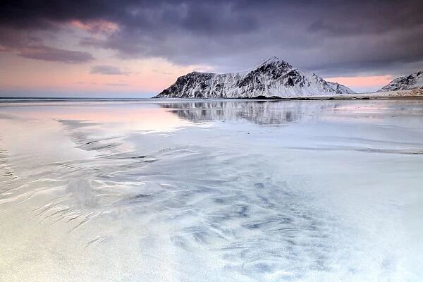 Sunset on Skagsanden beach surrounded by snow covered mountains reflected in the cold sea