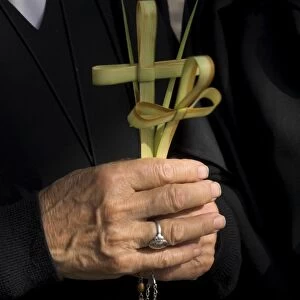 Close up of a nuns hands holding two crosses made of palm leaves
