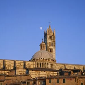 Moon in the sky above cathedral and houses clustered below at sunset