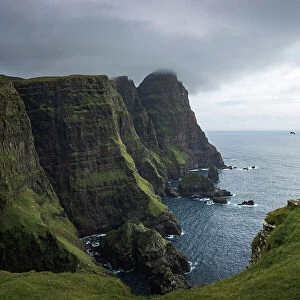 A hiker walking along the huge cliffs on the west coast of the islands of Suðuroy. In the backgound the cliff of Beinisvorð. Faroe Islands