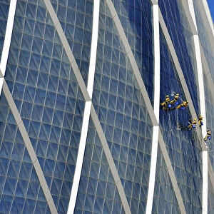 Window cleaners hanging on The Coin building Aldar headquarters, one of the largest