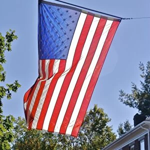 USA, Massachusetts, Lexington. Flags catch the sunlight over a brick home in Lexington