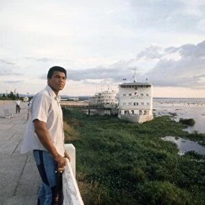 MUHAMMAD ALI (1942- ). NÔÇÜ Cassius Clay. American heavyweight boxer. Photographed on the shore of the Congo River at Kinshasa, Zaire, September 1974. The hospital ship Mama Mobutu and the presidential yacht President Mobutu are moored in the background at right