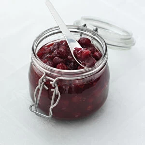 Cranberry sauce in glass jar, with a spoon resting on top, close-up