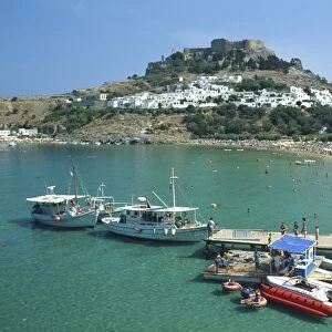 Greece, Rhodes, the acropolis overlooking Lindos town and bay, jetty with moored boats in foreground