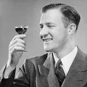 Smiling man holding up short glass with drink, (B&W), close-up