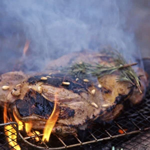 Leg of lamb, butterflied to flatten being barbecued on charcoal grill with rosemary
