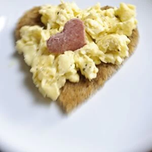 Valentines day breakfast of scrambled eggs on heart shaped toast with slice of salami