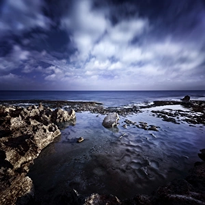 Rocky shore and tranquil sea against cloudy sky, Sardinia, Italy