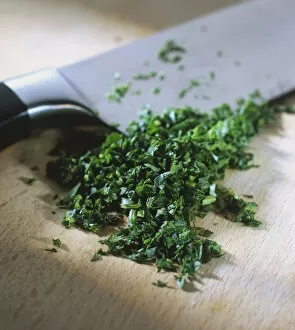 Petroselinum crispum, finely chopped Parsley leaves and a knife on a wooden board, close up